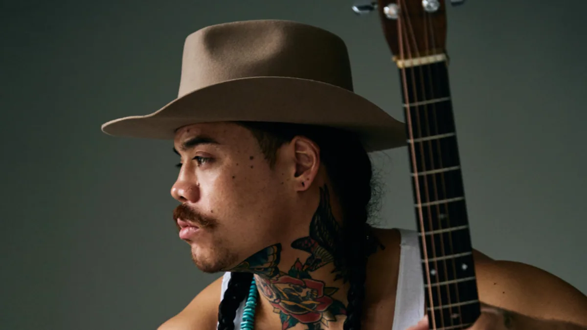 Logan Staats wearing a wide-brim hat and holding an acoustic guitar
